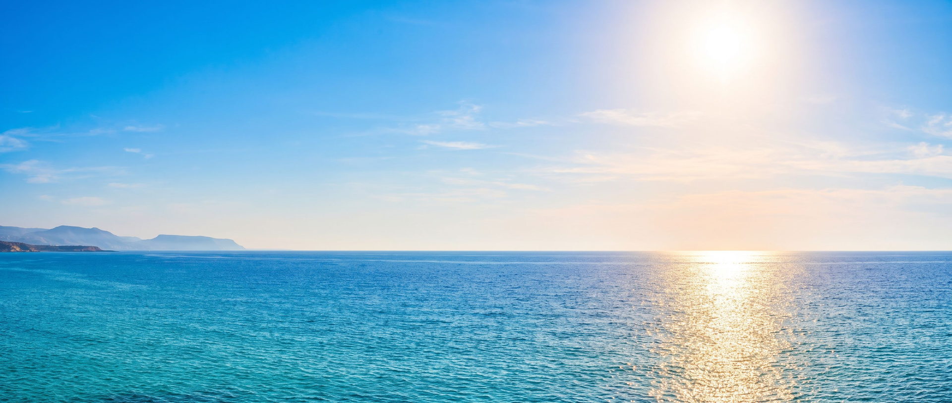 Weites Mittelmeer am Morgen vor Zypern: strahlend blauer Himmel, die Sonne zeichnet rechts einen goldenen Glitzerpfad aufs Wasser, links liegt die Küste im Dunst